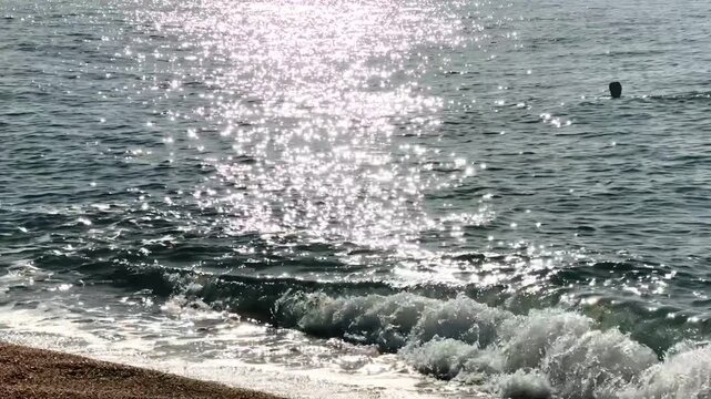 Sandy beach with sunlit sea and distant swimmers, video