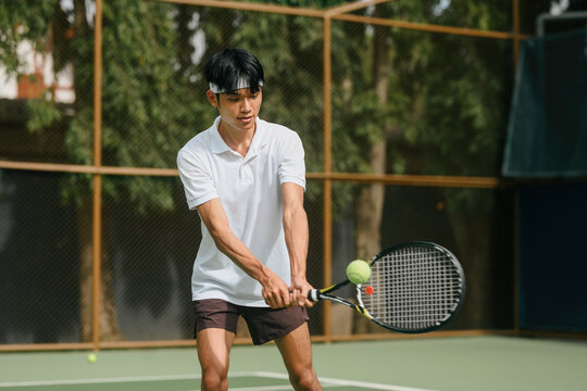 Young Asian Man Playing Tennis Outdoors, Hitting Backhand Shot on Court