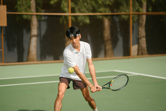 Young Asian Man Playing Tennis Backhand Shot on Outdoor Green Court