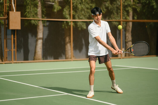 Young Asian Man Playing Tennis Backhand Shot on Outdoor Green Court