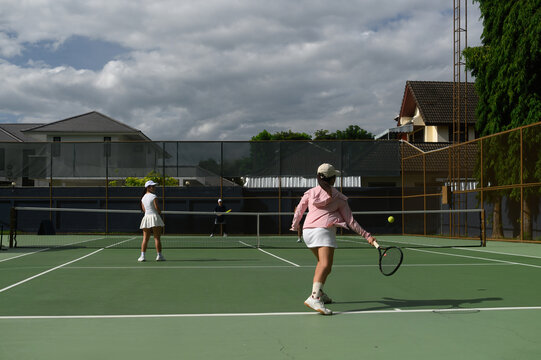 Wide angle of Women Playing Tennis on Outdoor Green Court with Cloudy Sky Background