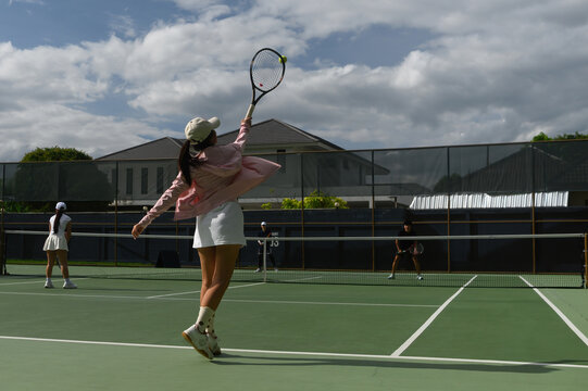 Wide angle of Young Asian Woman Serving Tennis Ball on Outdoor Green Court During Doubles Match