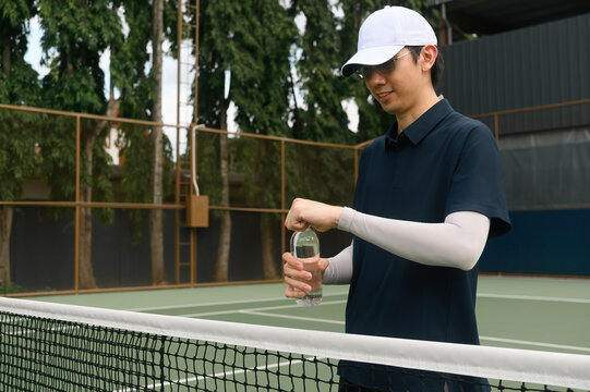 Asian Male Tennis Player Opening Water Bottle on Outdoor Court During Break