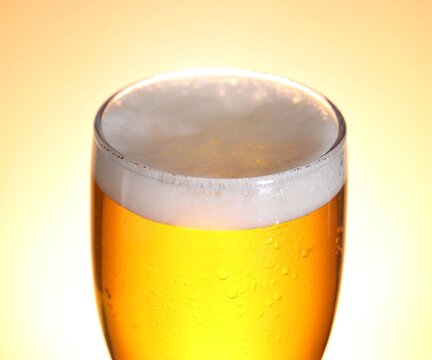 Glass with fresh beer on pale orange gradient background, closeup
