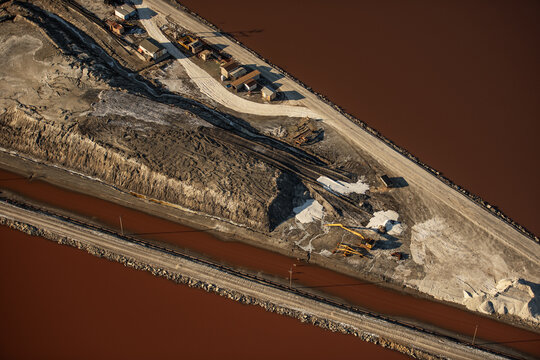 Aerial view of salt ponds and industrial infrastructure along the San Francisco Bay with reddish water, dirt roads, and construction equipment in Newark, California, United States.