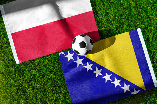 Poland vs. Bosnia and Herzegovina football match. National flags on green grass with soccer ball in the middle. Football background for international match.