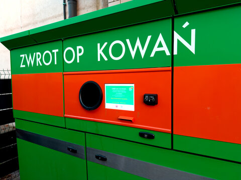 Modern green and orange reverse vending machine for bottle and can returns featuring a digital touchscreen display and circular intake opening on a city street