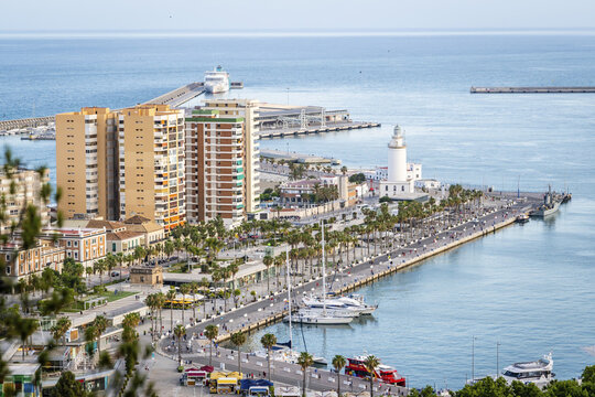 Aerial view of the port of Malaga featuring the historic La Farola lighthouse, palm-lined promenades, docked yachts, and modern buildings in Malaga, Andalusia, Spain.