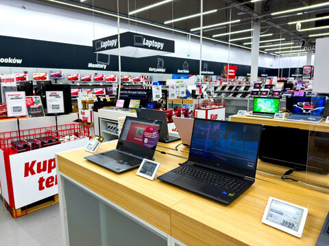 Modern electronics retail store interior with laptops and notebook computers on wooden display counters in a bright and spacious consumer technology shopping environment