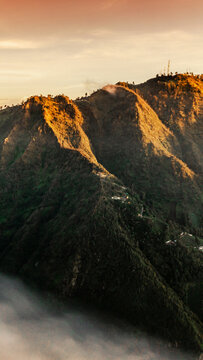 Aerial view of Mount Bromo at golden hour with mist covering the volcanic landscape in Tosari, East Java, Indonesia.
