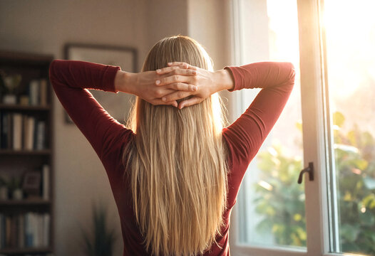 Woman Stretching Arms Back Relaxing Near Sunlit Window Inside Home