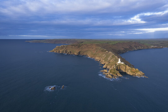 Aerial view of Start Point Lighthouse situated on a rocky headland surrounded by the sea under a dramatic cloudy sky in Start Point, England, United Kingdom.