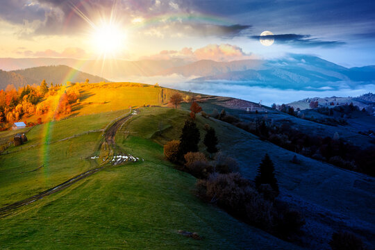scenic Carpathian landscape in autumn. day meet night. sun and moon over countryside mountain scenery with forest in fall colors. path through rolling hills in to the foggy valley under epic sky