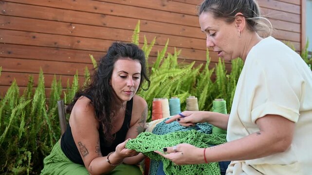 Female artisans discussing handmade crochet textile art outdoors,  video 4k real time