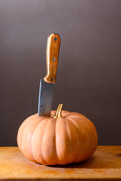 orange pumpkin on the wooden table. autumn vegetable harvest. dark background for thanksgiving or halloween carving concept. huge old knife stick in the vegetable