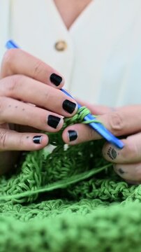 Female artisan crocheting green yarn with hook outdoors
