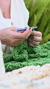 Female artisan crocheting green yarn with hook outdoors