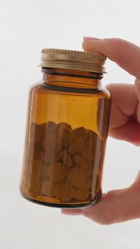 Amber glass supplement jar with golden metal cap held by female hand for womens healthcare vitamin d3 magnesium wellness and aging concept vertical slow motion video