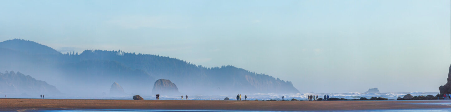 Beautiful wide panoramic view of a wild ocean coast with misty forested mountains and tiny people