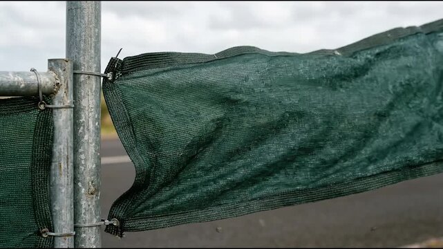 Dark green mesh panel billowing across metal scaffolding frame of temporary construction site hoarding barrier