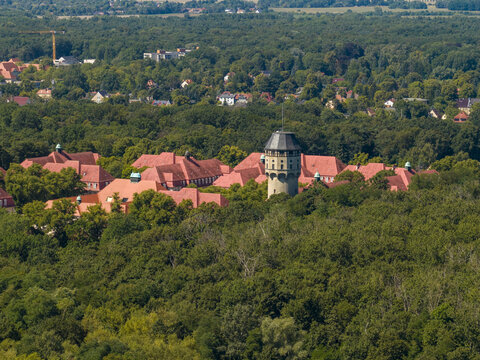 Aerial view of the historic Buch water tower surrounded by red-roofed buildings and dense forest in Berlin, Berlin, Germany.