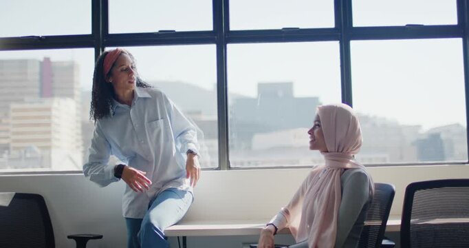 Female staff by office window headband woman leading talk while hijab woman listening sharing work