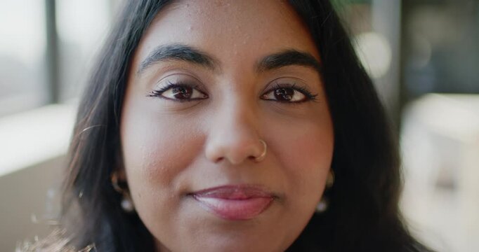 Indian woman blinking, smiling and holding gaze beside window at cafe with nose hoop