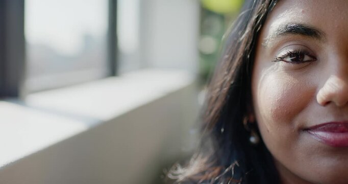 Adult Indian woman blinking then smiling, gazing at window with city view, pearl earring