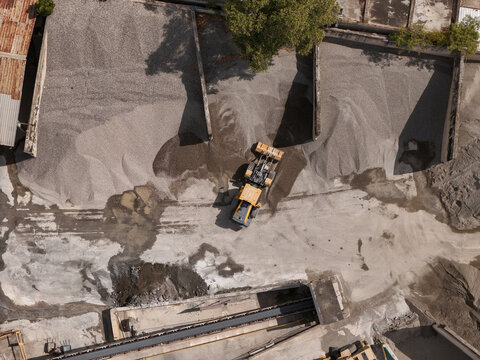 Aerial view of a yellow front-end loader moving gravel at a construction site with concrete partitions in Santo Domingo, Distrito Nacional, Dominican Republic.
