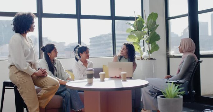 Female coworkers watching central speaker opening laptop and leading meeting at office lounge