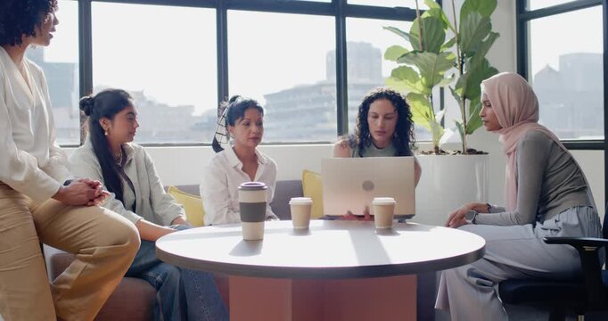 Diverse female team meeting at table by windows curly opening laptop presenting rest sipping coffee