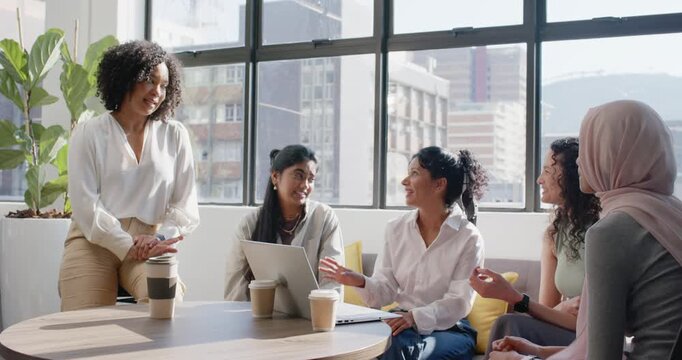Diverse female team listening as standing woman leading ideas with laptop and to-go cup in lounge