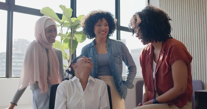 Diverse female coworkers laughing after seated woman's laugh, turning to camera at office windows