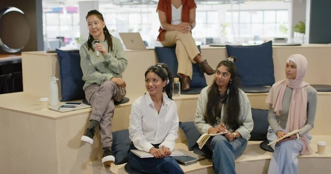 Diverse team with microphones and notebooks, responding to presenter speaking in office, applauding