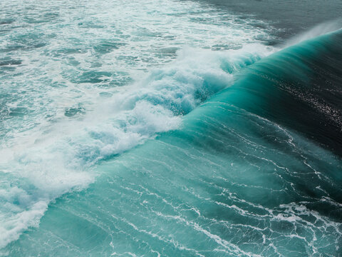 Aerial view of a powerful turquoise ocean wave breaking with white sea foam and deep blue water in Dee Why, New South Wales, Australia.