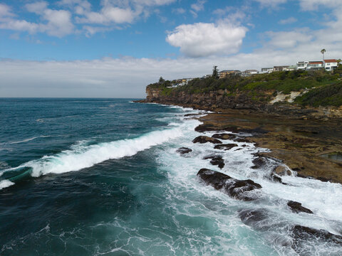 Aerial view of the rugged coastline at Dee Why with waves crashing against rocky shores and residential houses perched on the cliffside in Dee Why, New South Wales, Australia.