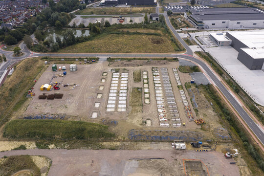 Aerial view of a BESS construction site featuring rows of concrete foundations and battery storage racks on a dirt lot near industrial facilities.