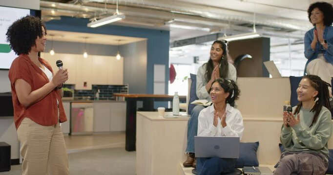 Diverse team clapping after African American woman speaker pausing at work talk with mic