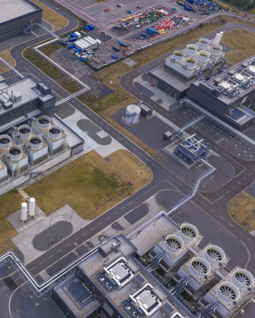 Aerial view of a modern hyperscale data center facility featuring rows of industrial cooling towers, complex piping systems, and paved access roads in Belgium.