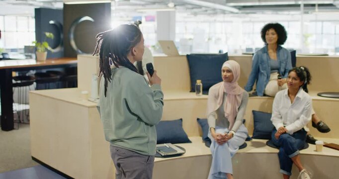 Nonbinary African American presenter entering tiered seating, leading meeting in office with mic