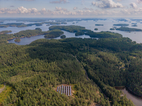 Aerial view of Haukivesi lake system featuring dense pine forests and a small solar panel array nestled among the trees in Rantasalmi, South Savo, Finland.