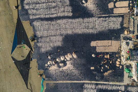 Aerial view of Gohira drying field with workers spreading fish on black plastic sheets in Anwara, Chittagong Division, Bangladesh.