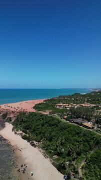 Vista a&eacute;rea de praia com quiosques e constru&ccedil;&otilde;es entre vegeta&ccedil;&atilde;o e fal&eacute;sias em Pipa, Rio Grande do Norte, Brasil, mar azul-turquesa e litoral potiguar filmado de drone, destino de turismo e viagem