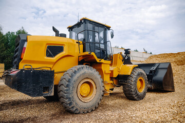 Fototapeta premium Yellow wheel loader parked on gravel surface with large pile of wood chips in the background, showcasing heavy machinery in an outdoor construction site