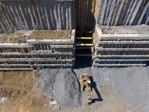Aerial view of a yellow excavator working in a deep construction excavation site with reinforced concrete walls and support beams in Istanbul, Istanbul, Turkiye.