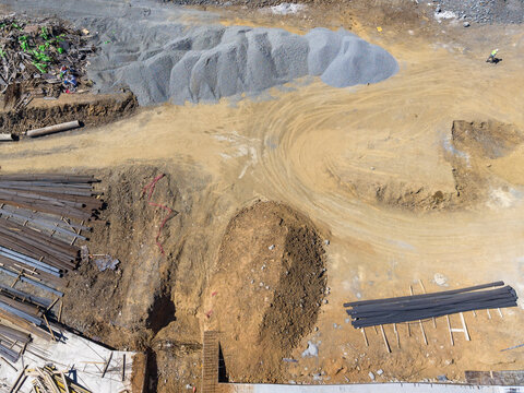 Aerial view of a construction site featuring piles of gravel, stacks of metal rebar, and dirt paths with a worker in a high-visibility vest in Istanbul, Istanbul, Turkiye.