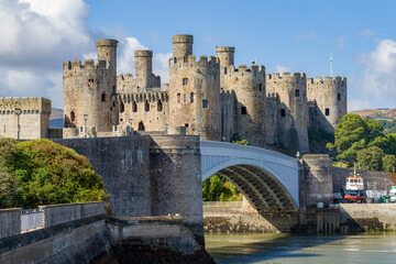 Obraz premium Medieval stone fortress towers and arched road bridge over tidal river estuary, historic coastal defensive fortification on sunny day
