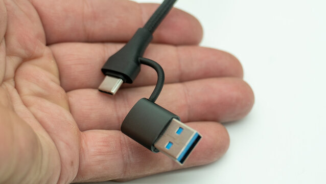 A person is holding a USB cable. One end features a USB-A connector&mdash;isolated against a white background&mdash;while the other has a USB-C connector. The open palm ensures the cable is clearly visible. 