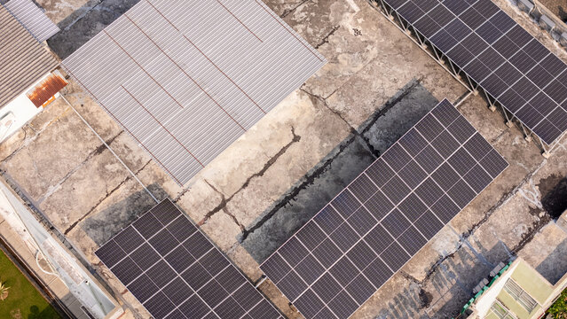 Aerial view of solar panels installed on a weathered concrete rooftop with a corrugated metal section in Klaten, Central Java, Indonesia.