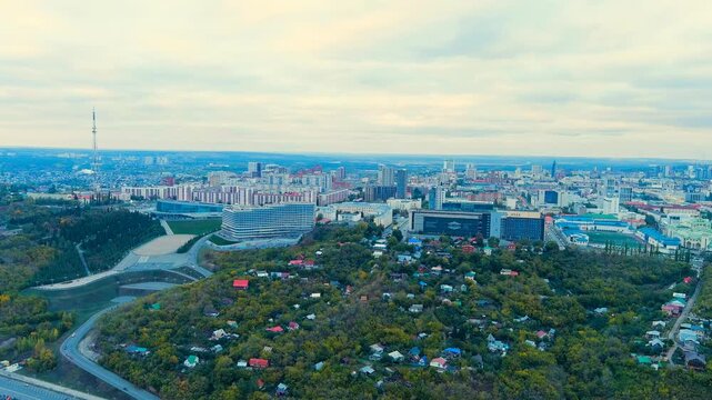 Ufa, Russia. Panoramic Drone footage of the central cityscape at twilight, modern and Soviet-era buildings rising above dense autumn woodland under a softly clouded sky. Drone footage
